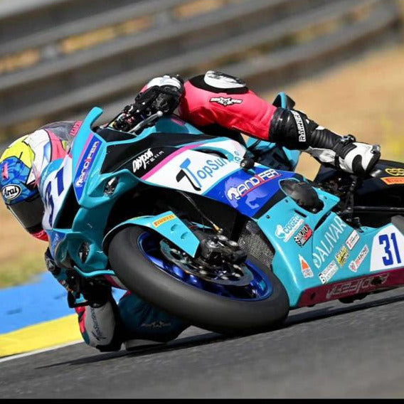 
                  
                    Alberto García pilotando una motocicleta Dalivar durante una carrera de superbike, inclinando la moto en una curva de circuito de velocidad.
                  
                